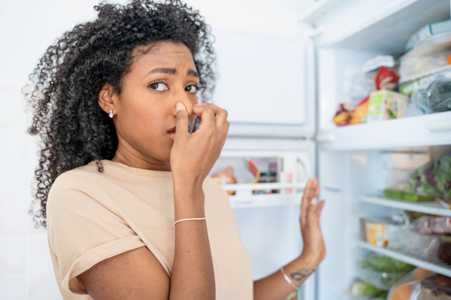 lady holding nose in front of an opened fridge